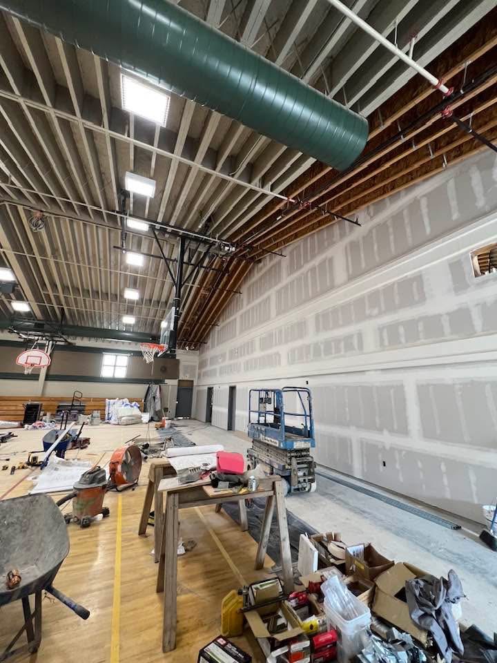 Gymnasium during drywall installation with lifts and scaffolding
